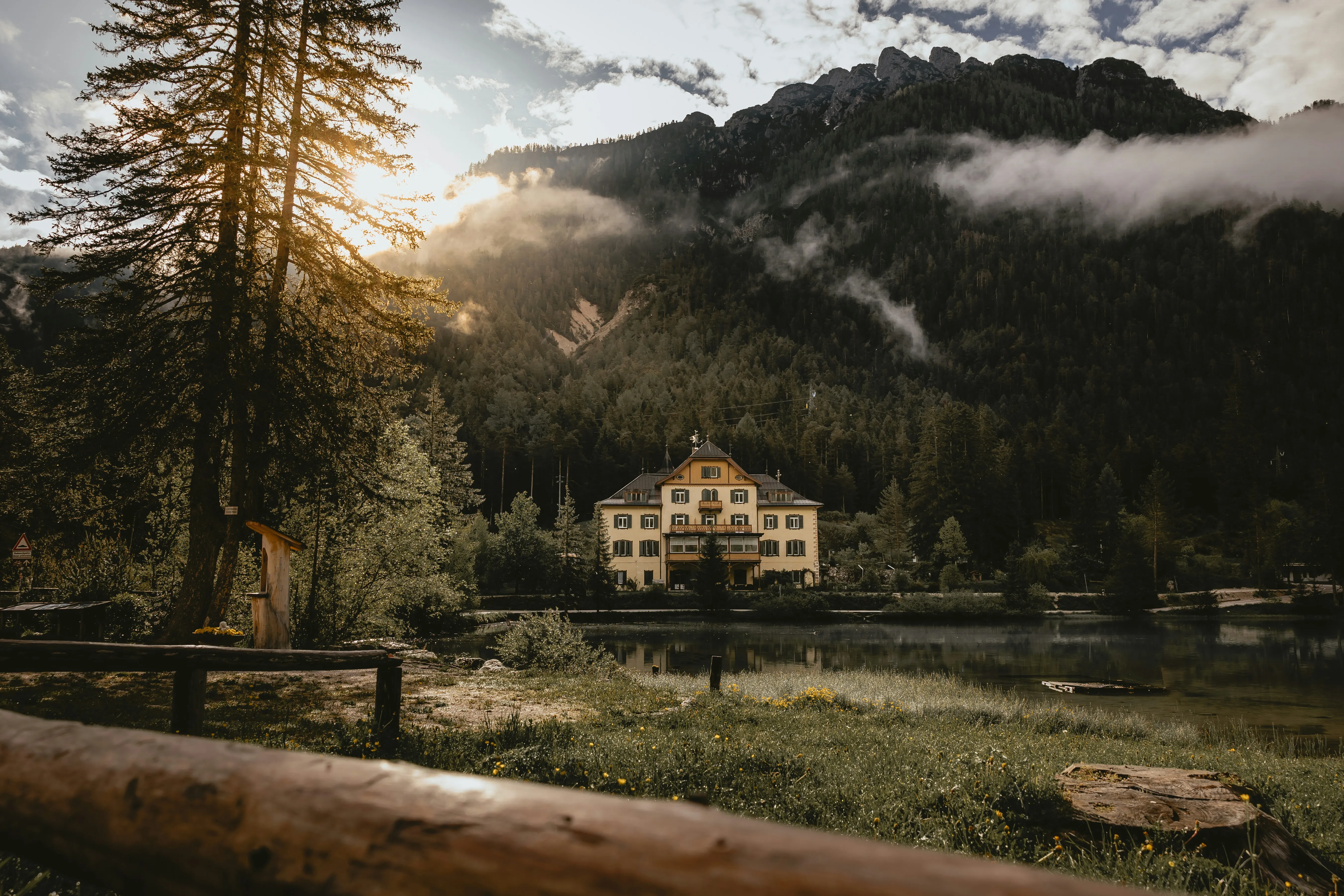 A grand alpine lodge beside a still lake in the Dolomites at golden hour